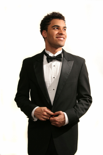 Stylish young man in a tuxedo holding a microphone, posing against a dark background with smoke, actor, singer, show, host of the event. Party concept.