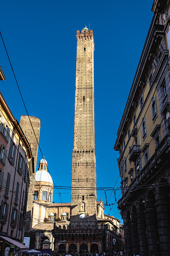 Bologna, Italy - March 5, 2023: Alley with old residential buildings, view on Two Towers against clear blue sky in Bologna, Italy