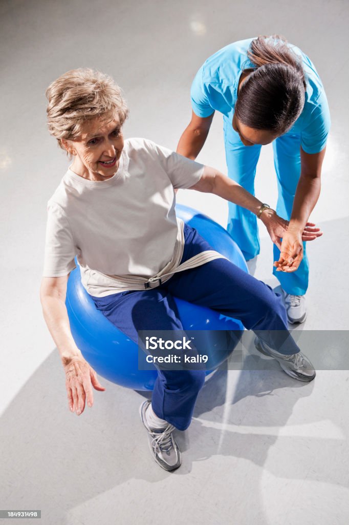 Physical therapist with senior woman on exercise ball "Physical therapist (40s) working with senior woman (80s), doing core strengthening exercises on stability ball." Balance Stock Photo