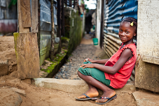 A young African girl leaning against a zinc shack.