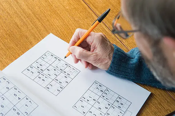 Senior man at desk doing a sudoku puzzle. Space for copy.