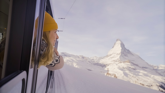 Woman traveler looking out through train window admiring beautiful winter landscape and snowcapped mountain
