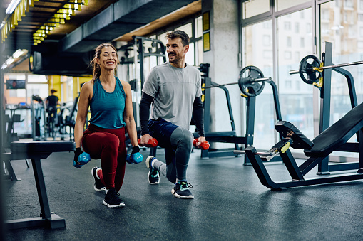 Happy athletic couple having weight training in lunge position at health club. Copy space.