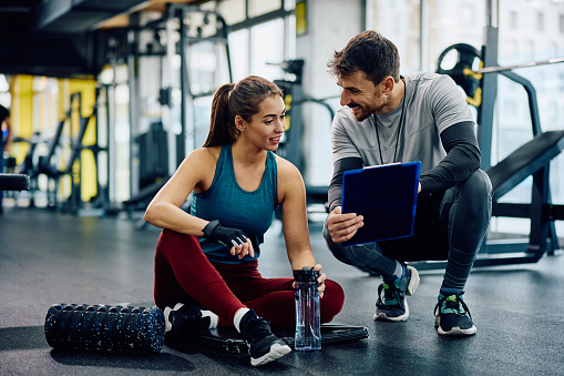 Young sportswoman and her fitness instructor analyzing workout plans in health club.