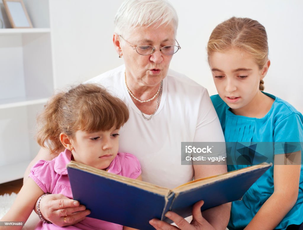 Grandmother Reading Book To Her Grandchildren Portrait of an family, grandmother reading old book to her granddaughters, looking at book and smiling 4-5 Years Stock Photo