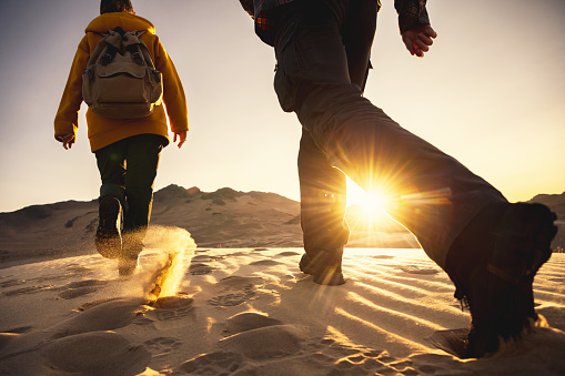 Two hikers with backpacks walks in sunset desert dunes. Close up photo of hiking boots. Hiking concept