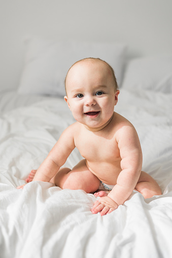 Smiling newborn baby on a white bed at home, the concept of a happy healthy infant baby. Generation alpha and gen alpha.