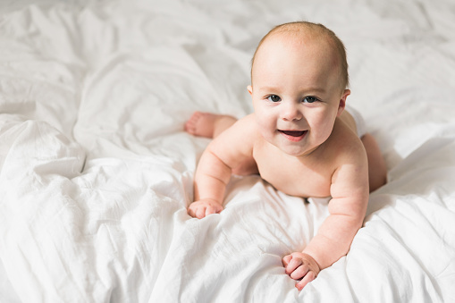 Smiling newborn baby on a white bed at home, the concept of a happy healthy infant baby. Generation alpha and gen alpha.