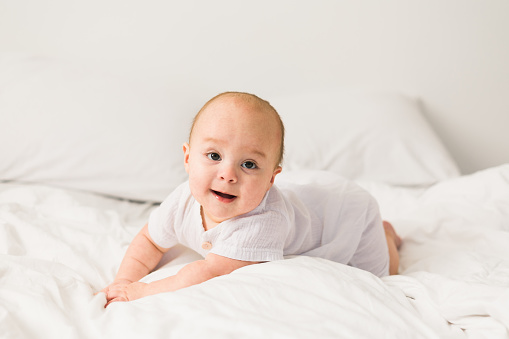 Adorable baby boy in white sunny bedroom. Newborn child relaxing in bed. Nursery for young children. Textile and bedding for kids. Family morning at home