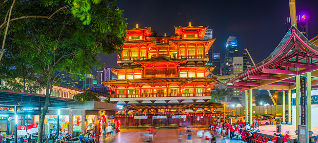 The crowded skyscraper cityscape of the Downtown Core overlooking the warmly illuminated Buddha Tooth Relic Temple in Chinatown, Singapore.