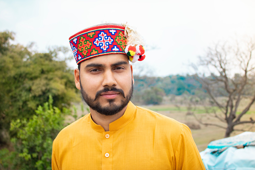 Outdoor portrait of a young man from Himachal Pradesh with traditional Himachali cap looking at the camera with a smile.