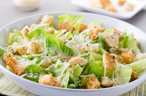 SEVERAL MORE IN THIS SERIES. Closeup of a fresh caesar salad, with romaine lettuce hearts, croutons, parmesan cheese and dressing.  Dressing and croutons in background.  Very shallow DOF.