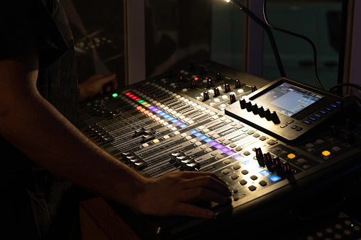 unrecognizable sound technician operating a multitrack mixing console in the control room during an event