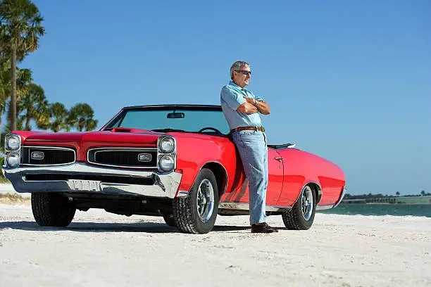 Senior adult on the beach with a restored 1967 convertible.