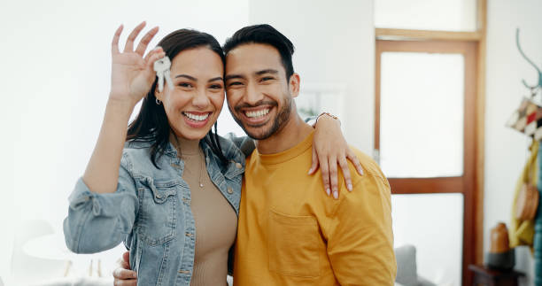 new home keys, hug and portrait of happy couple moving into house, real estate property or apartment purchase. love, homeowner smile and mexican man, woman or relocation people embrace in living room - reduction looking at camera finance business imagens e fotografias de stock