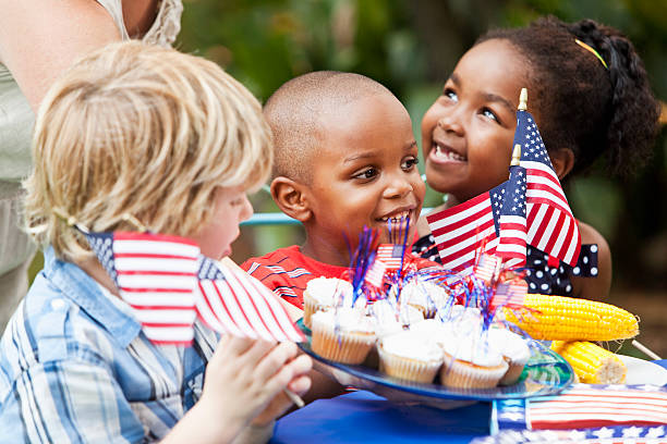July 4th or Memorial Day picnic celebration Woman serving cupcakes to excited children (6, 4 and 7 years) at July 4th cookout.  Focus on boy in middle. independence day holiday photos stock pictures, royalty-free photos & images