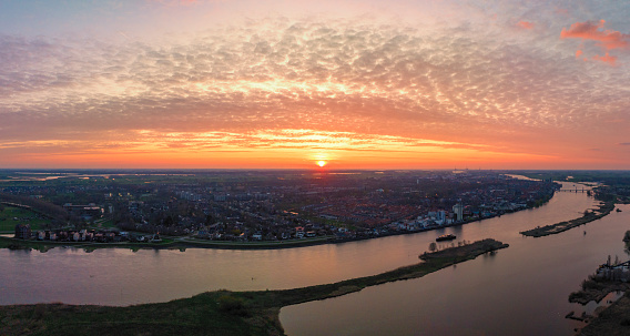 Panoramic aerial view on Kampen and the river IJssel in the IJsseldelta during a springtime sunset in Overijssel. The flow of the river is leading towards the setting sun in the distance while lights are popping up in the city at the end of a beautiful springtime day.