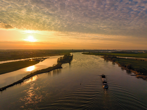 Panoramic aerial view on the river IJssel and Reevediep Bypass waterway during a springtime sunset in Overijssel. The flow of the river is leading towards the setting sun in the distance while lights are popping up in the city at the end of a beautiful springtime day.