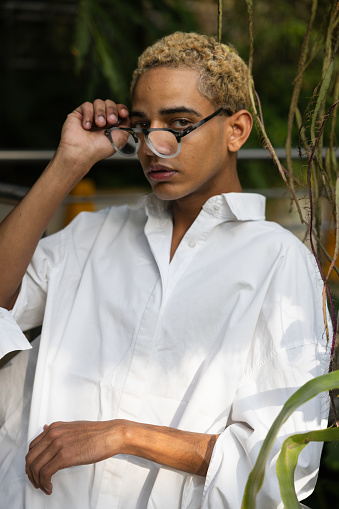 Beautiful black young man with glasses looking at camera, in greenhouse, copy space