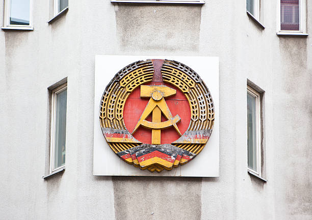 Emblem of former German Democratic Republic Emblem of the former German Democratic Republic with the communist symbols od hammer and sickle and spikes around. This emblem is attached to a house near former Checkpoint Charlie, a border patrol between Eastern and Western Berlin. east germany stock pictures, royalty-free photos & images