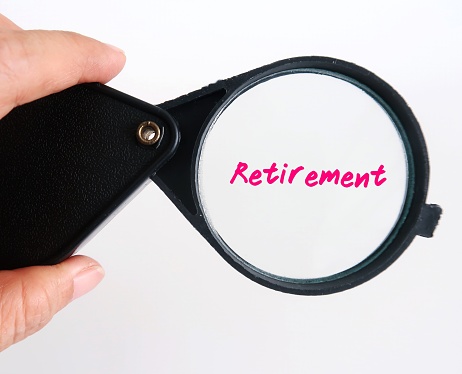 Hand holding magnifying glass focus on the text written RETIREMENT, on white background with copy space. Concept of focusing on life after ones active working life