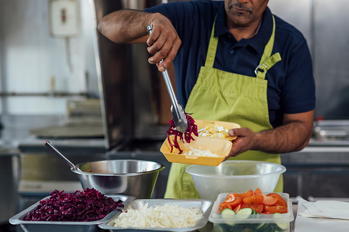 Man running a small takeaway business in North Yorkshire, England. He is preparing food in the kitchen, adding salad to a meal.