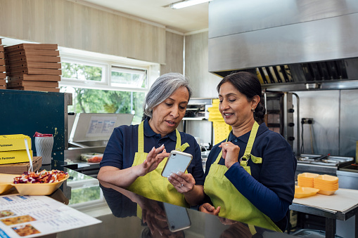 Employees working at a small takeaway business in North Yorkshire, England. They are preparing food in the kitchen, using a mobile phone, talking.