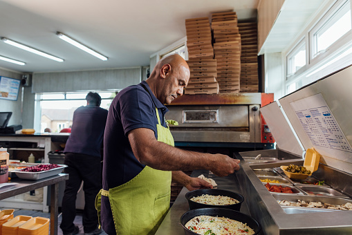 Side view of a man running a small takeaway business in North Yorkshire, England. He is preparing food in the kitchen, making pizzas.