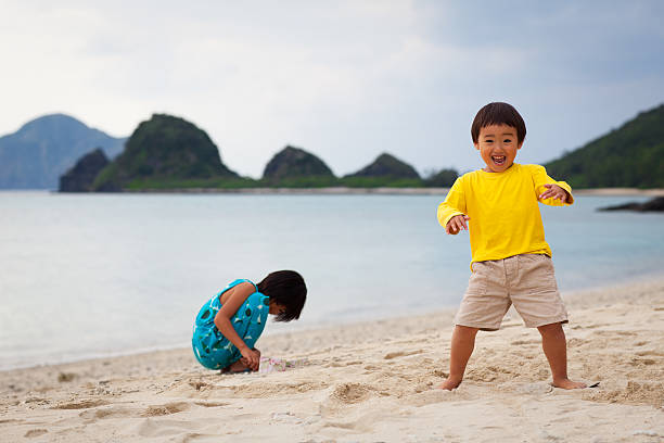 Asian siblings play and look for shells on the beach.