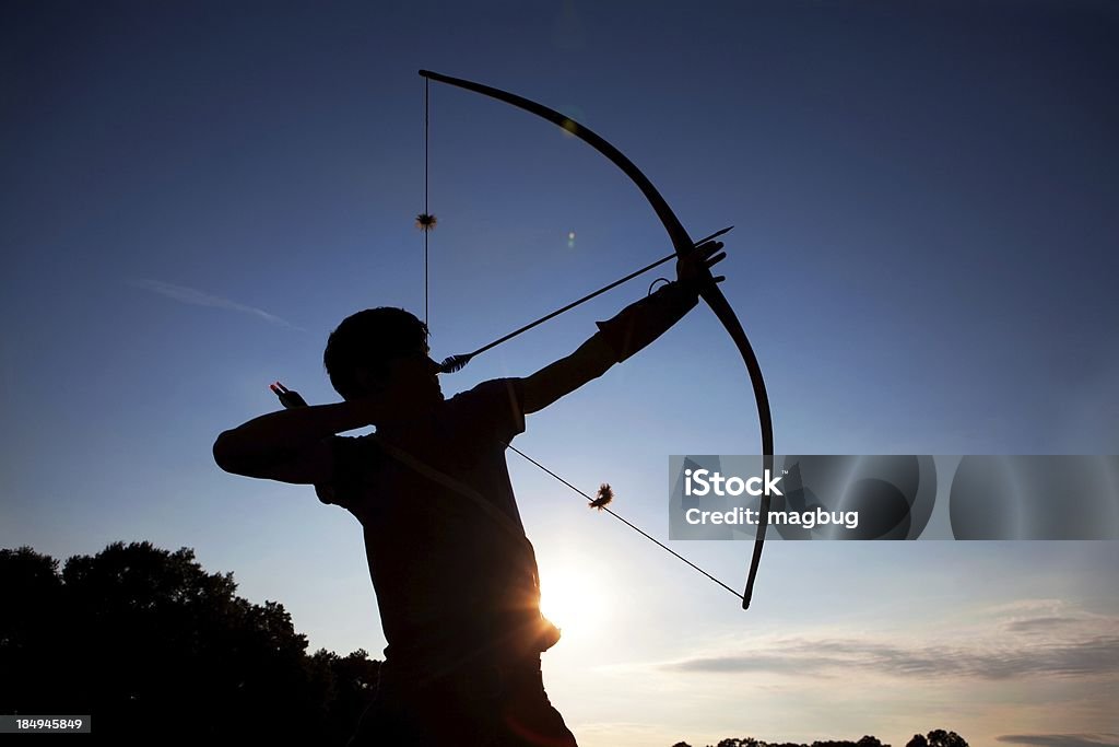 Aiming HIgh Young man in silhouette taking aim  with his bow and arrow at sunset Bow and Arrow Stock Photo