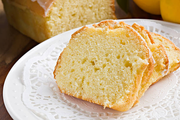 Pound Cake "A high angle close up of several slices of lemon pound cake laying on a white doily placed over a plate, the rest of the loaf and a couple of ripe lemons can be seen in the background." pound cake stock pictures, royalty-free photos & images