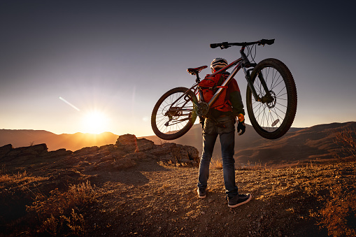 Male mountain biker goes uphill and carry a bicycle on his back to sunset mountain