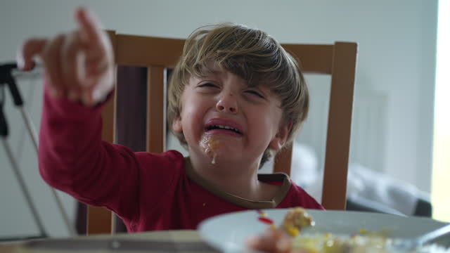 Small boy having a tantrum at lunch table. close-up face of child hitting table and crying displeased and with messy mouth