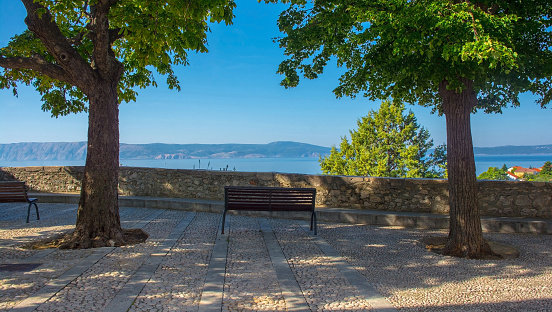A bench overlooking the sea in the Stari Grad historic centre of the coastal town of Novi Vinodolski, Primorje-Gorski Kotar County, Croatia. Krk Island is visible across the Adriatic Sea