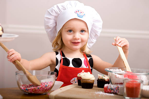Cтоковое фото Капкейк украшая by Маленькая девочка в шляпе шеф-повара и фартук