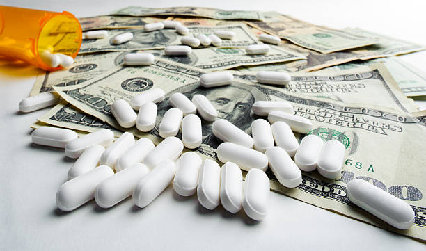 Medicine and Money Several medicine pills are spread across many U.S. Dollars. Concept of drugs and money.See more Medicine & Science images: meds and money stock pictures, royalty-free photos & images
