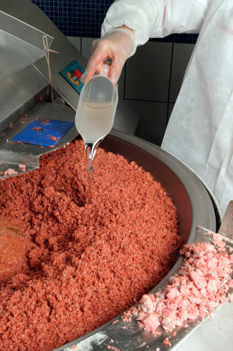 Butcher is mixing meat and spices to make salami in food processing plant..