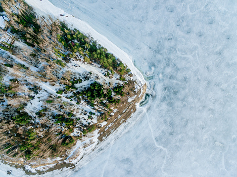 Aerial view of frozen lake water and snow winter woods. Beautiful winter landscape, drone view