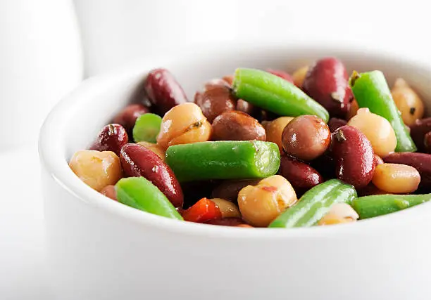 "Colorful mixed beans salad in a white bowl, on a white background, selective focus."