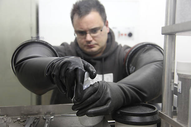 Young scientist working in a glove box "Young scientist opening a plastic bottle in a glove box. Please, see also:" glove box stock pictures, royalty-free photos & images