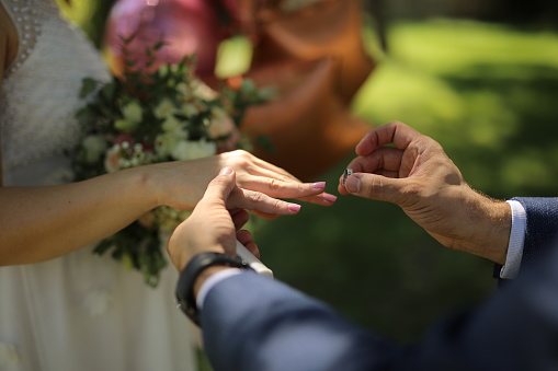 Groom standing in front of bride and putting ring on her finger, close up