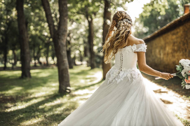 Back view of bride spinning in a wedding dress on green field Back view of beautiful bride spinning in a wedding dress on green field while holding bridal bouquet bride holding bouquet stock pictures, royalty-free photos & images