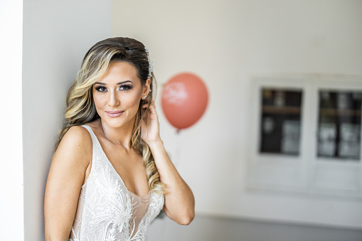 Portrait of beautiful bride leaning on wall and posing on wedding day while looking at camera