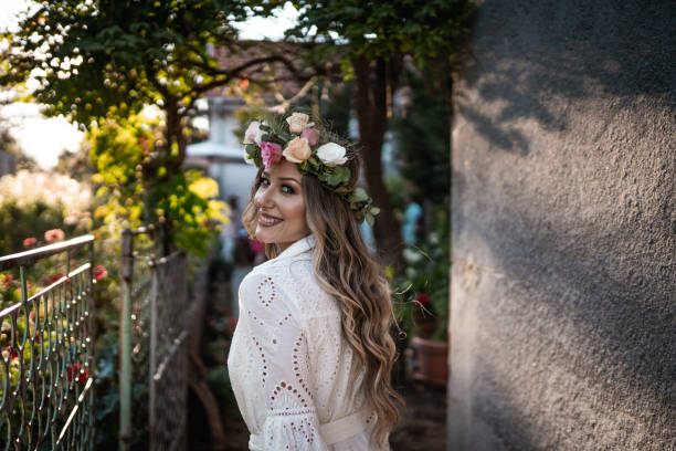 mariée souriante en robe avec couronne florale marchant dans la cour arrière et logging à la caméra par-dessus l’épaule - caméra à lépaule photos et images de collection