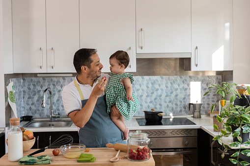 young father in the kitchen holding his baby in his arms while preparing a delicious lunch