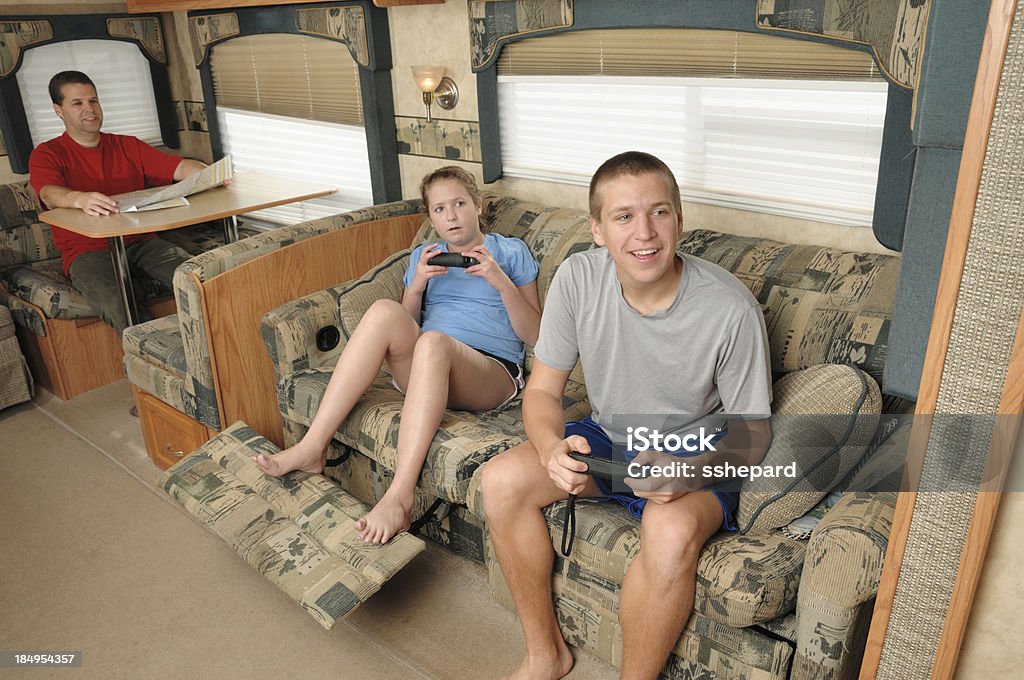 Family enjoying recreational vehicle "Brother and sister enjoying video game in recreational vehicle living room while dad looks on while planning trip with road map, horizontal." Adult Stock Photo