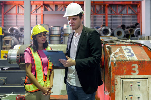 istock Two people, wearing hard hats, are standing together inside a factory, discussing their work. 1849573914
