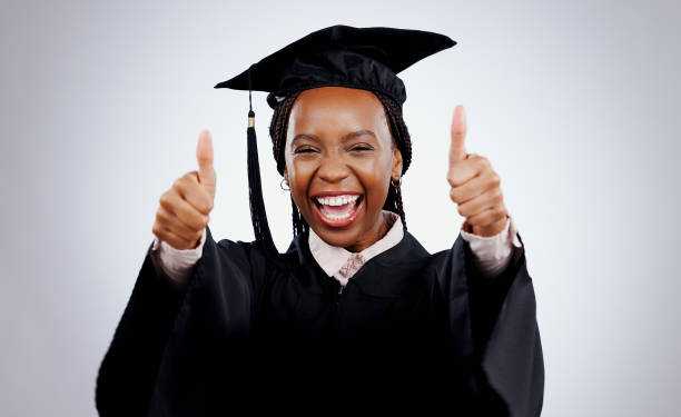 istock Graduation cap, woman and thumbs up for study success, celebration and education, learning or college in studio. Portrait of excited African graduate or student with like emoji on a white background 1849585778