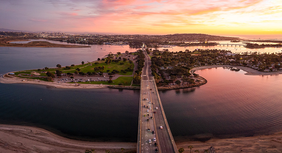 Savor the mesmerizing hues of a scenic sunset over Mission Bay in San Diego. This panoramic aerial view captures the beauty of the iconic drive bridge gracefully crossing the tranquil waters