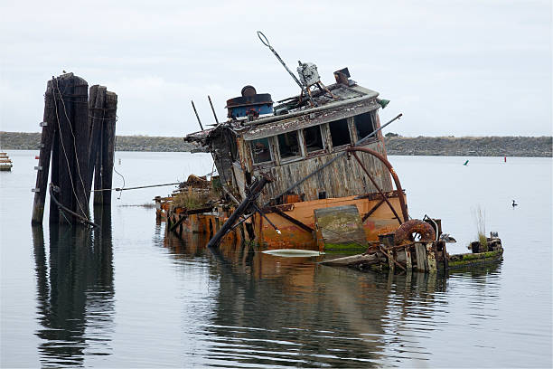 Sinking and decaying boat in Gold Beach Oregon Harbor "Half-sunk, decaying boat in Gold Beach Oregon Harbor under overcast skies" fishing boat sinking stock pictures, royalty-free photos & images
